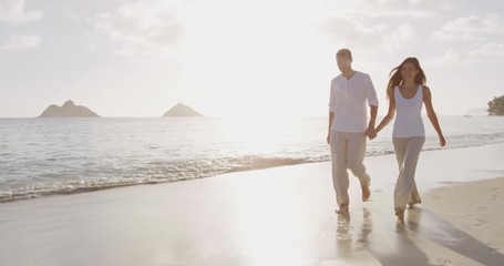 Beach sunset couple walking romantic on honeymoon on Hawaii. Sunrise romance young couple in elegant casual clothing walking together enjoying travel vacation holidays on Lanikai beach, Oahu, USA. - Powered by Adobe