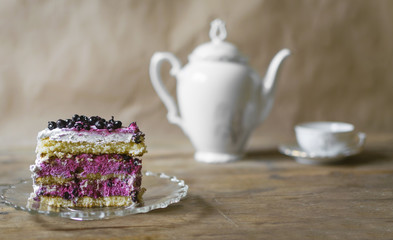 Piece of blueberry cake on wooden table with cup of tea in background