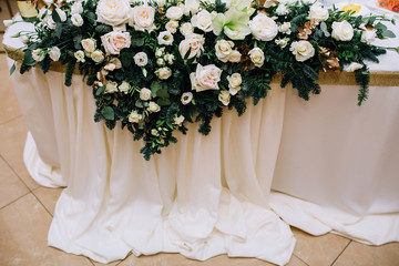 composition of roses, eustoma of white color, fir, pistachio on the wedding table of a newly-married couple covered with a white cloth