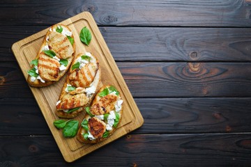 Italian restaurant menu, food background. Appetizing bruschetta with grilled chicken, ricotta and basil flat lay on wooden table with free space