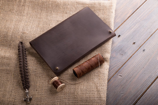 leather dark brown purse on a dark wooden background, with a thread and a needle.