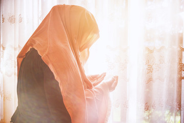 Muslim woman with hijab praying indoor at bright window