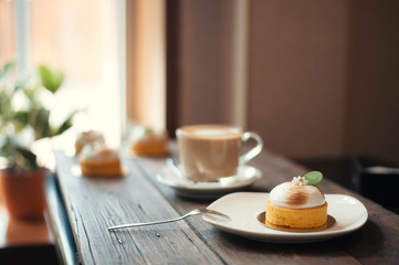 On the wooden table there is a saucer with pancake, fork and coffee