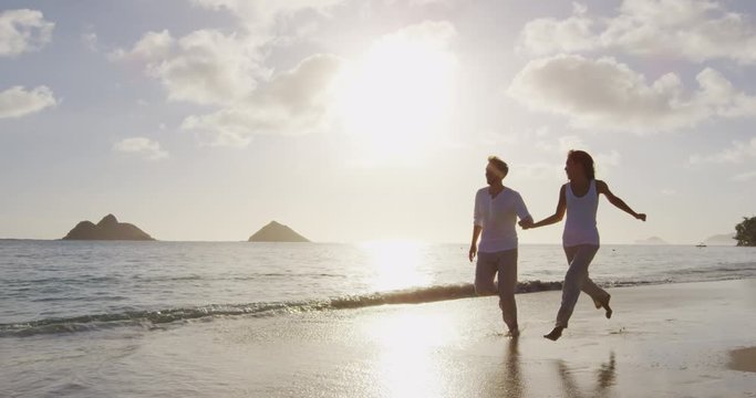 Couple at beach at sunset romantic holding hands running playful. Young couple in love enjoying romance in casual elegant clothing on luxury beach vacation travel holidays, Lanikai, Oahu, Hawaii