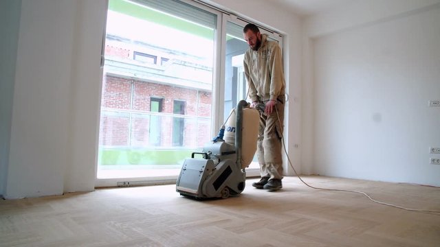 Sanding hardwood floor with the grinding machine. Repair in the apartment. Carpenter doing parquet wood floor polishing maintenance work by grinding machine
