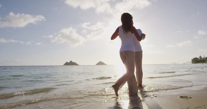 Romantic couple walking at beach at sunset dancing around holding hands. Young couple in love enjoying romance in casual elegant clothing on luxury beach vacation travel holidays, Lanikai, Oahu Hawaii