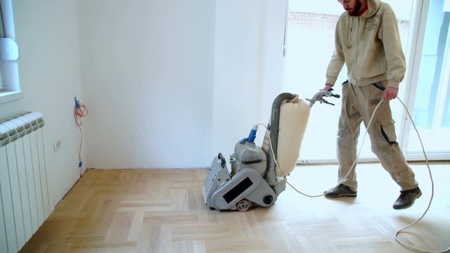 Sanding hardwood floor with the grinding machine. Repair in the apartment. Carpenter doing parquet wood floor polishing maintenance work by grinding machine
