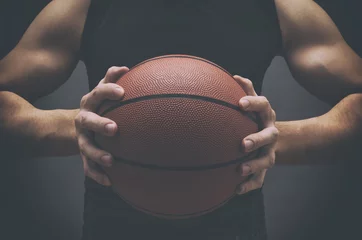  Male basketball player with a ball over dark background. Fit young man in sportswear holding basketball. © NatasaAdzic