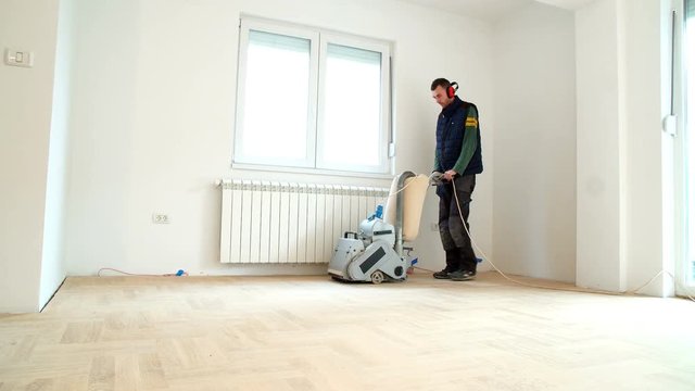 Sanding hardwood floor with the grinding machine. Repair in the apartment. Carpenter doing parquet wood floor polishing maintenance work by grinding machine