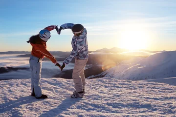 Foto op Plexiglas Wintersport Lovely couple holding hands in shape of heart on snowy peak at sunset. Winter vacation