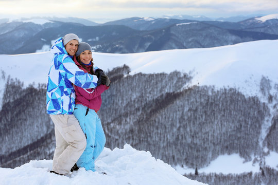 Happy couple on snowy mountain peak at resort. Winter vacation