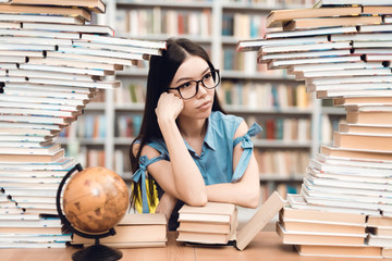 Ethnic asian girl sitting at table surrounded by books in library.