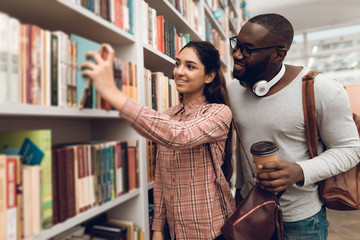 Ethnic indian mixed race girl and black guy in library. Students are looking for books.