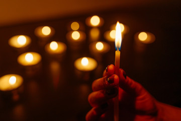 Kemerovo, Russia, fire in the mall, burning candles. Candle in female hands on black background. Many candles burning at night. Many candle flames glowing on dark background. Close-up. Free space.