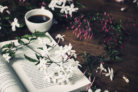 jasmine flowers, open book and a cup of coffee on a wooden table