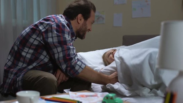 Loving dad tickling happy daughter and wishing good night before sleep, bedtime