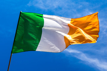 Irish flag fluttering in a brisk breeze against a bright blue sky