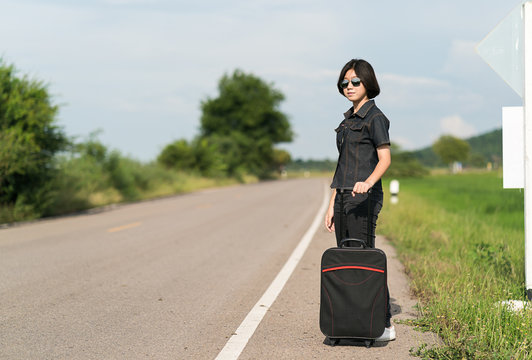 Woman with luggage hitchhiking along a road