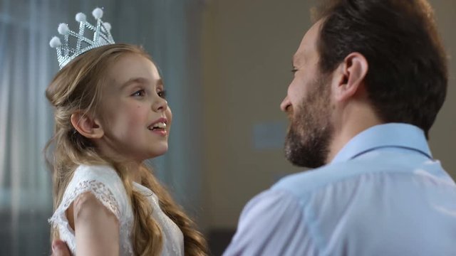 Cute little girl in princess crown dress hugging father, tender relations, party