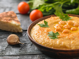Freshly made hummus in a clay bowl on a table with a piece of bread.