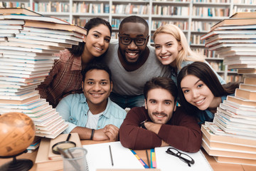 Six ethnic students, mixed race, indian, asian, african american and white surrounded with books at...