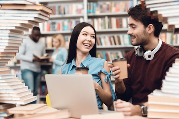 Ethnic asian girl and white guy surrounded by books in library. Students are using laptop.