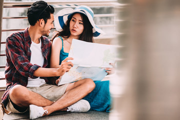 Couple Asian travelers are sitting on city street and looking at interesting places to travel from paper map. Vacation Concept. . Travel concept