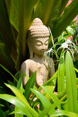 Stone statue of Buddha stands in the thickets of tropical flowers North Goa.India  