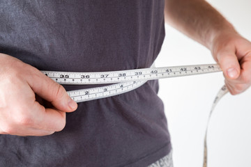 Slim man measuring his waist. Healthy lifestyle, body slimming, weight loss concept. Cares about...