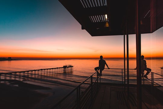 Silhouette of men sitting on pier railing and watching sunset