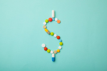 Symbol of money dollar from colored pills and capsules on  green background. Expensive medicine and...