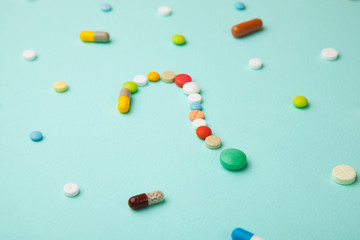 Symbol question mark from colored tablets and capsules on  green background. What medicines to choose better, what will help