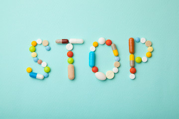 Word STOP from colored pills and capsules on  green background. Medicines and tablets kill