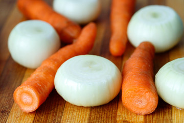 on a cutting board in a stripe are onions and carrots are cleaned and not sliced, juicy and bright vegetables