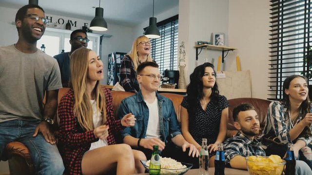 Mixed race friends watching popular TV show. Medium shot. 4K slow motion. Singing, laughing and smiling group. Emotion.