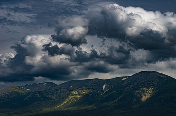 Obraz na płótnie Canvas Scenic stormy cloudscape over mountains peaks with sunny highlights on the slopes