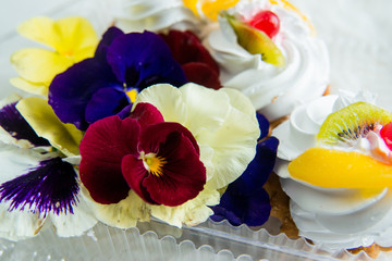 dessert: cake with fresh fruit and edible flowers (pansies) on a light background. the concept of natural nutrition, the use of colors in cooking