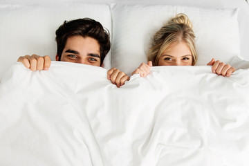 Young loving couple lying on the bed, peaking 
