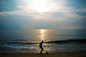 Lad playing football suring sunset on seashore