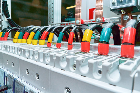 A range of electrical wires or cables are connected to the power circuit breakers. Black wires are marked in different colors. In the background, the design of the electrical Cabinet with busbars.