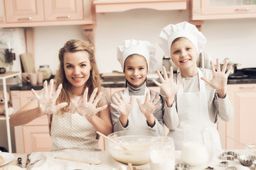 Children with mother in kitchen. Family is showing on camera hands in flour.