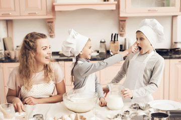 Children with mother in kitchen. Family is playfully smearing dough on nose.