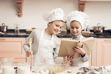 Children in kitchen. Brother and sister are reading cookbook while cooking.