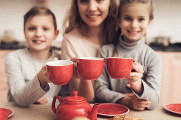 Children with mother in kitchen. Family is holding cups with tea.