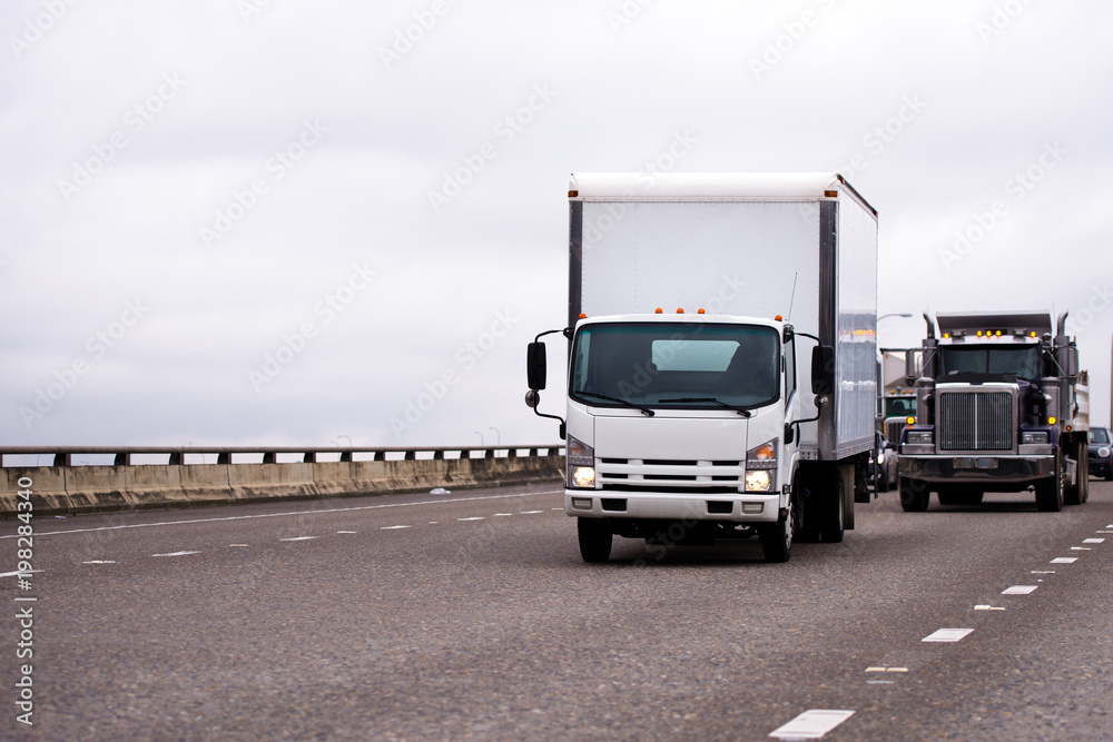 Wall mural Small semi truck with box trailer and big rig classic semi truck running on wide highway with traffic