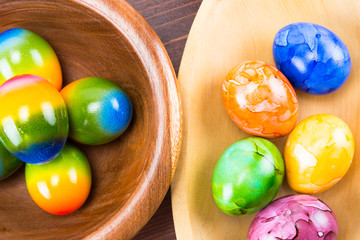 Colored by hand Easter eggs in a natural oak and ipe wood bowls isolated on a ipe wood counter top board close up