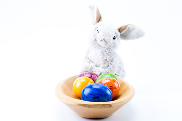 Easter bunny on a wood bowl holding hand painted easter eggs with white background front view