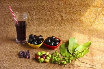 Jamun juice glass and bowls of Jamun fruit or black plum, raw Jamun fruits, leaves and seeds