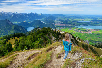 Fototapeta premium Cute little hiker enjoying picturesque views from the Tegelberg mountain, a part of Ammergau Alps, located nead Fussen town, Germany.