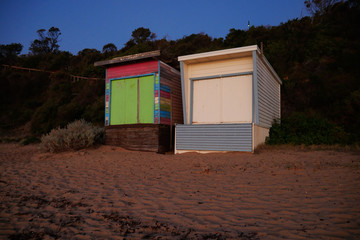 Obraz na płótnie Canvas A pair of old beach boxes glow orange from a setting sun on a warm summer evening on the Mornington Peninsula in Victoria, Australia